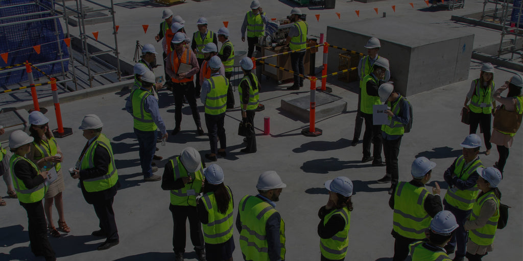 Gathering of a large group of construction workers wearing head protection and high visibility gear.