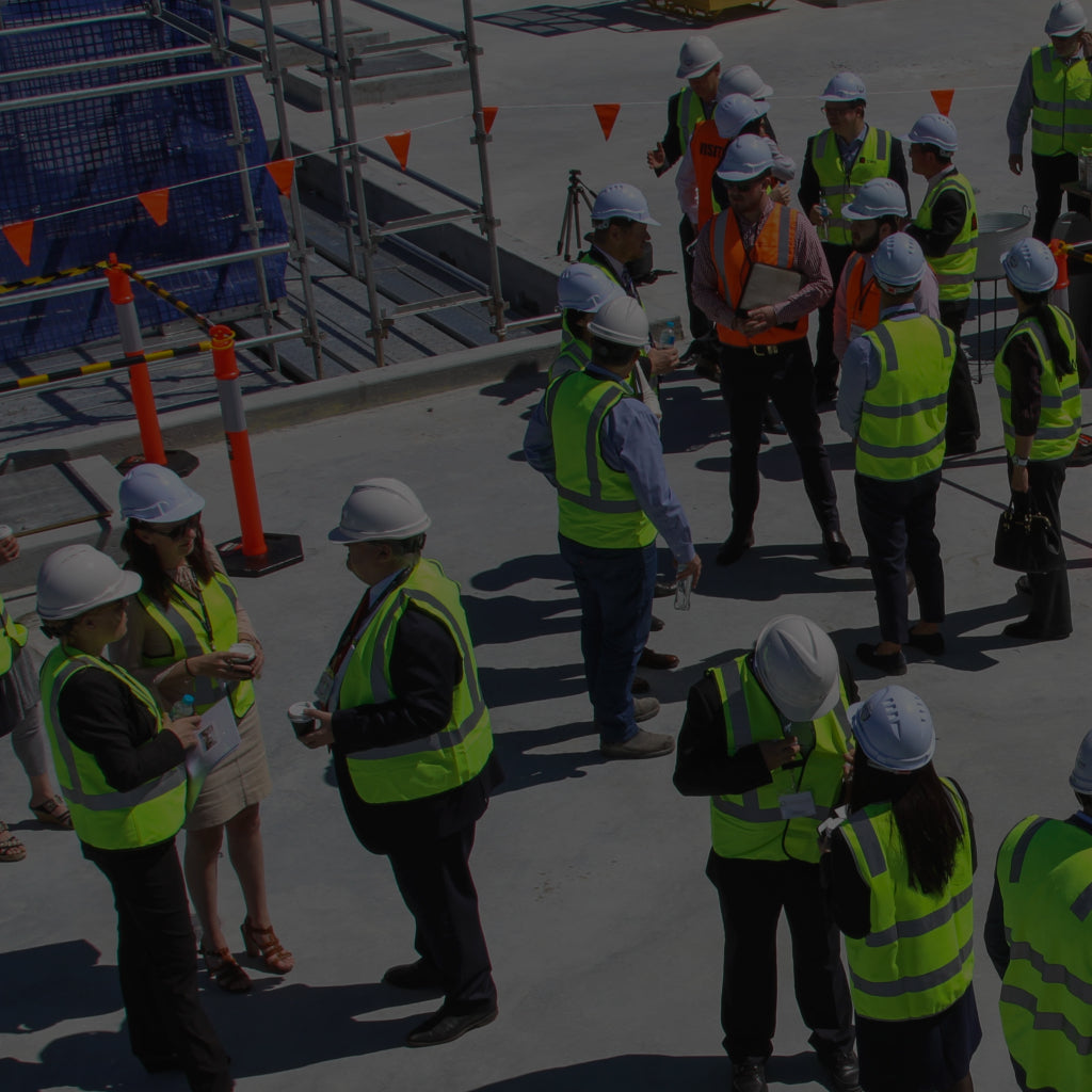 Gathering of a large group of construction workers wearing head protection and high visibility gear.