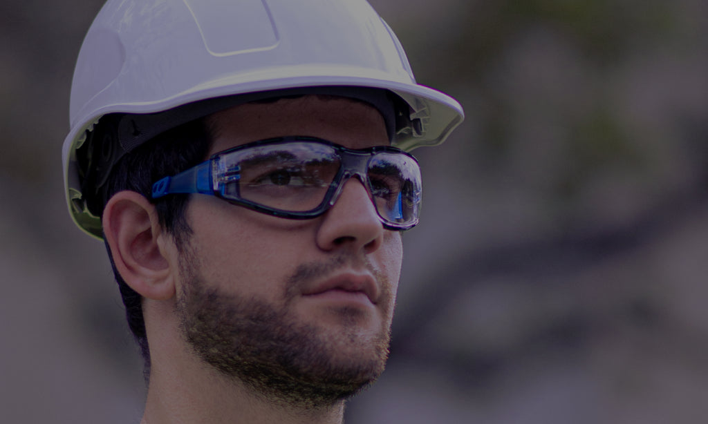 Construction worker wearing a Jorestech white cap-style hard hat with a 6-point ratchet suspension system to protect his head from falling objects. He is also wearing clear high-impact safety glasses that are shatter resistant and anti-fog. The classes have a removable foam gasket for extended protection to the sides of the eyes, and rubberized temple legs for extended comfort during long term wear.