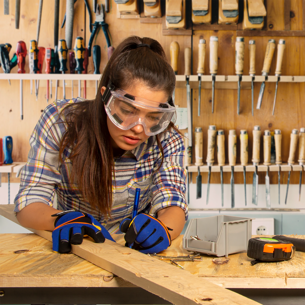 Image of a woman wearing anti-fog ventilated safety goggles while working in with wood and wood tools in her art studio
