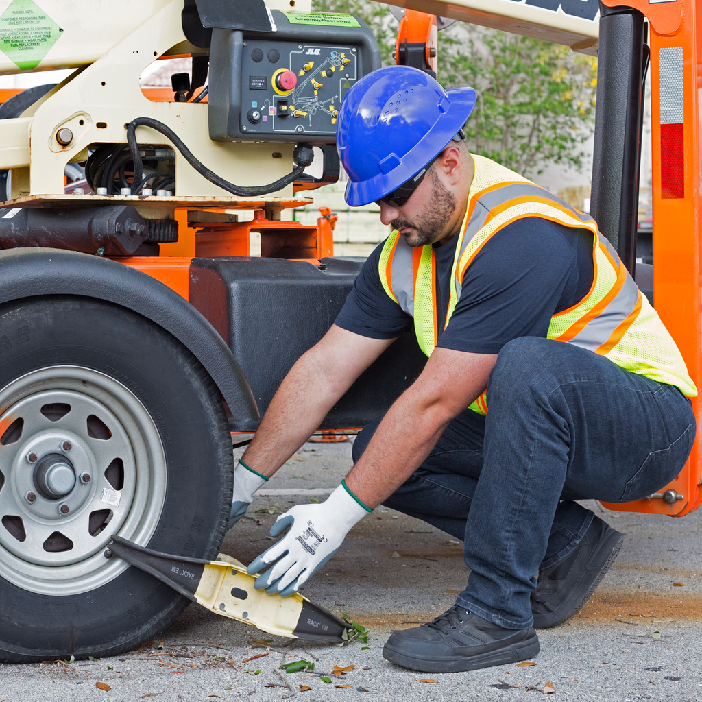 A man putting brakes onto the wheels of a crane. He is wearing a blue Jorestech full brim safety hard hat, safety gloves and a high visibility vest