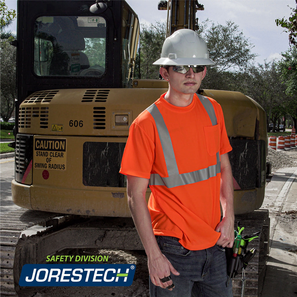 Worker wearing a heat transfer short sleeve orange safety shirt while doing road work. There is a very large truck on the background.