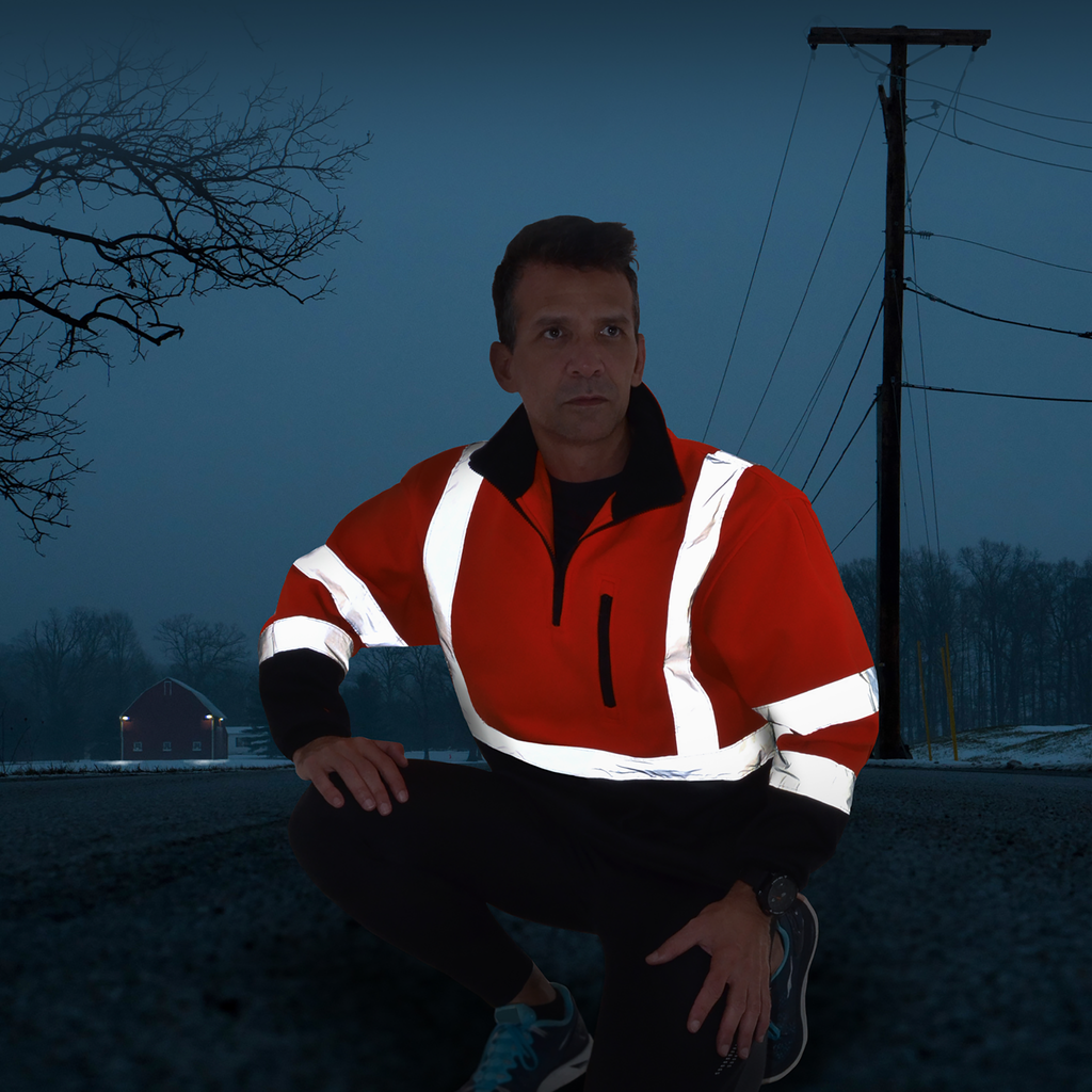 Image of a person wearing the Hi-vis JORESTECH  safety sweater. The action takes place during night time and the reflective stripes are very bright and visible. A house is in the distance with lights on and 