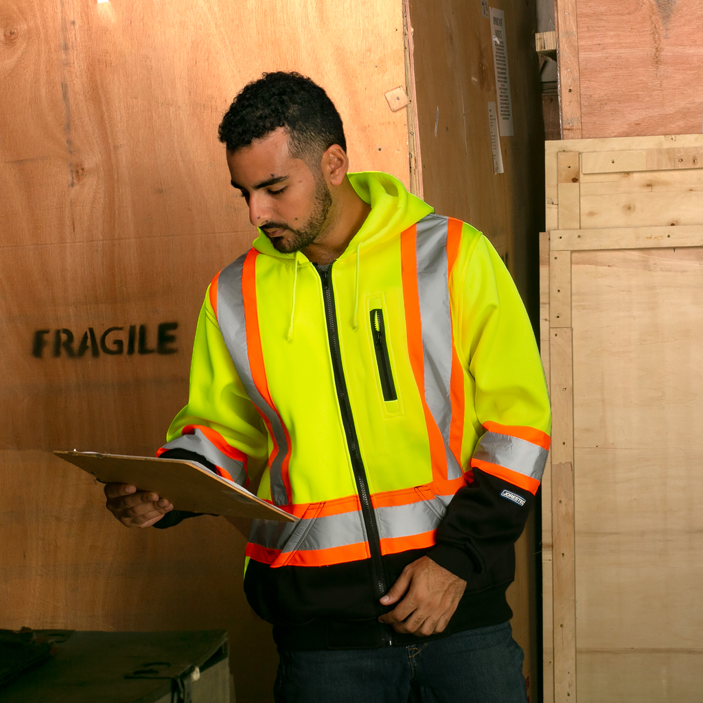 Image of a worker wearing the Yellow black safety hooded sweatshirt with reflective and contrasting orange stripes organizing merchandize in wood boxes marked as fragile