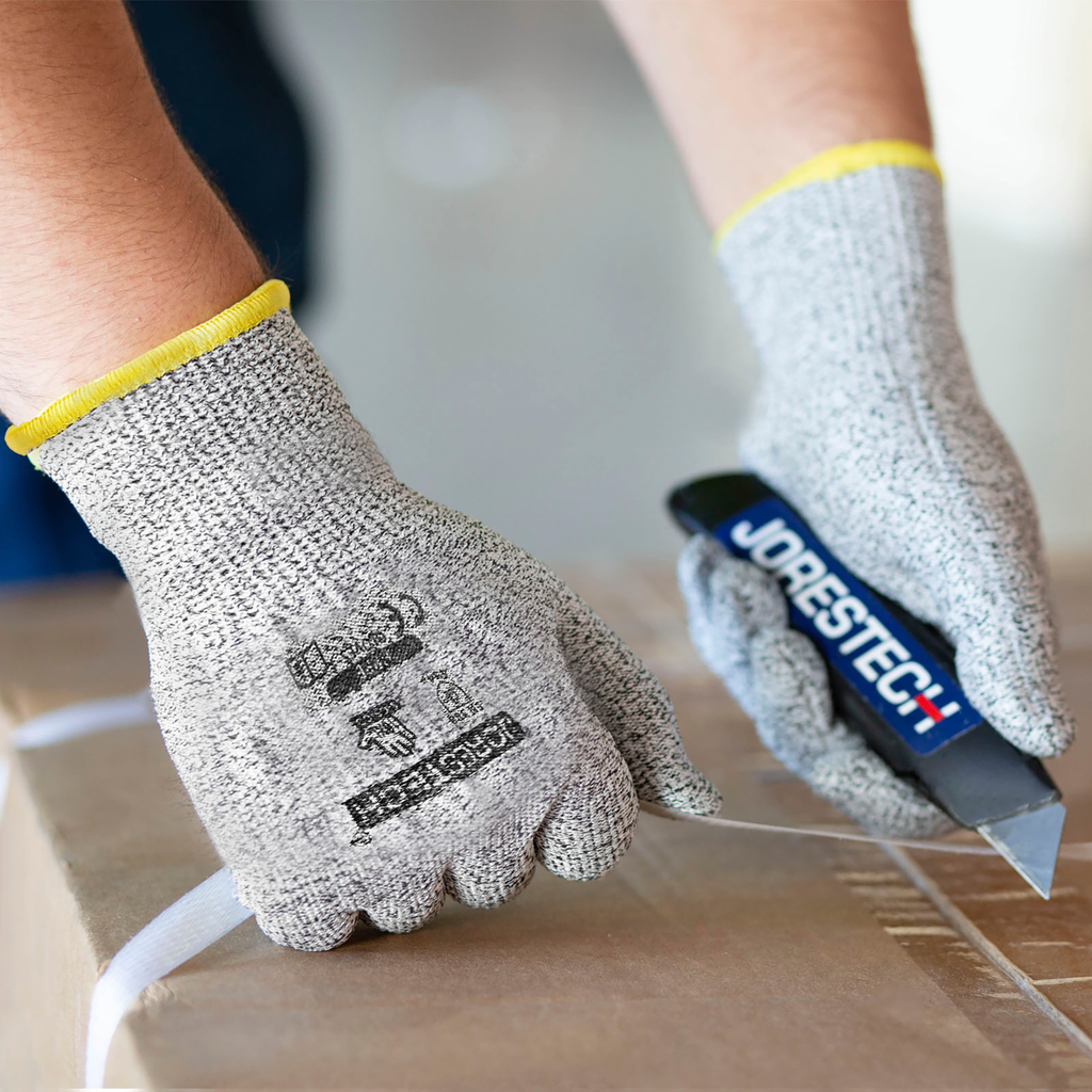 Hands of a person wearing the Jorestech multi purpose safety work glove while cutting a strap with a box cutter