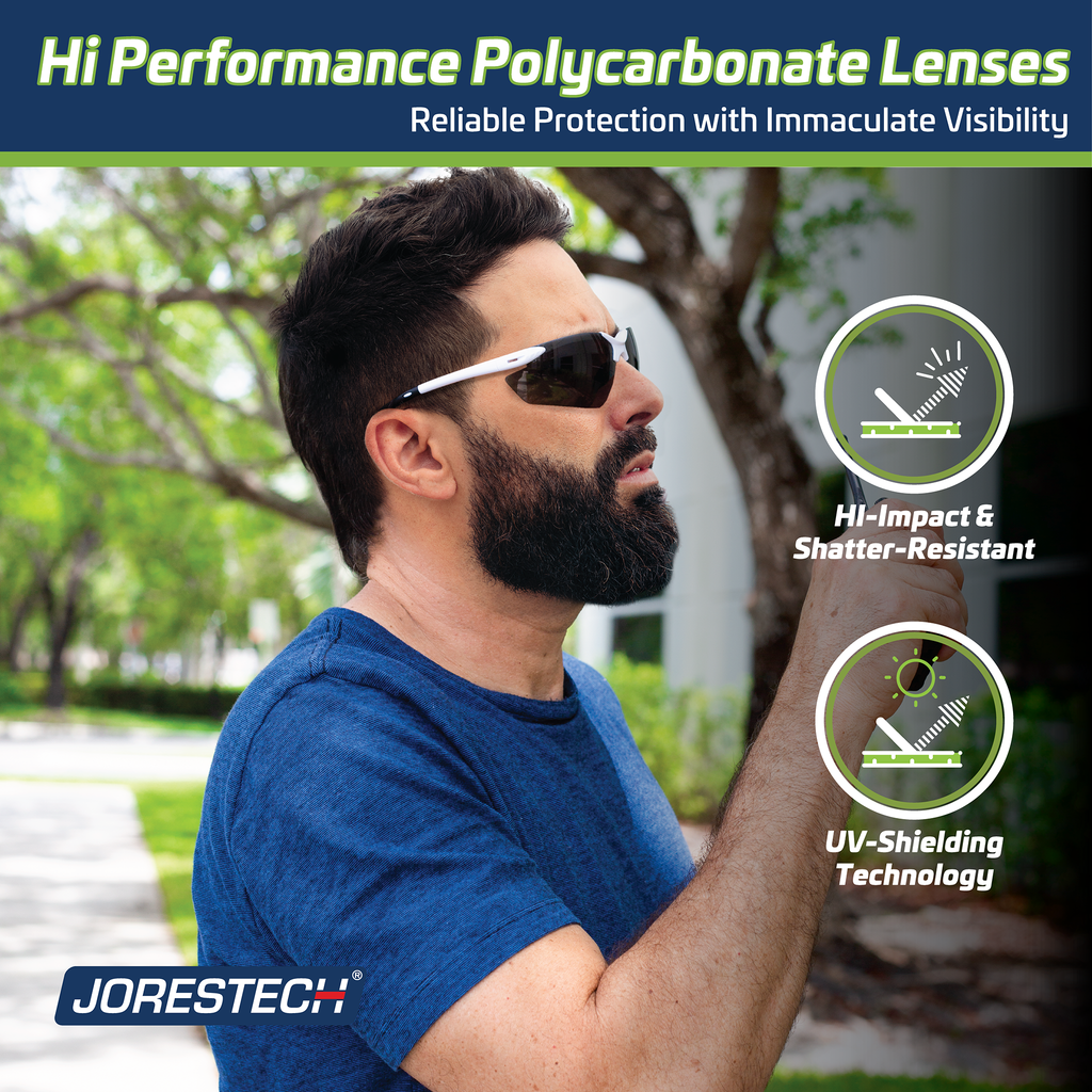 A worker talking on a portable radio wearing the Jorestech hi impact smoke wrap around ANSI Z87+ safety glasses. Text read: Hi performance polycarbonate lenses, reliable protection with immaculate visibility. Hi Impact and shatter resistant, UV Shielding technology