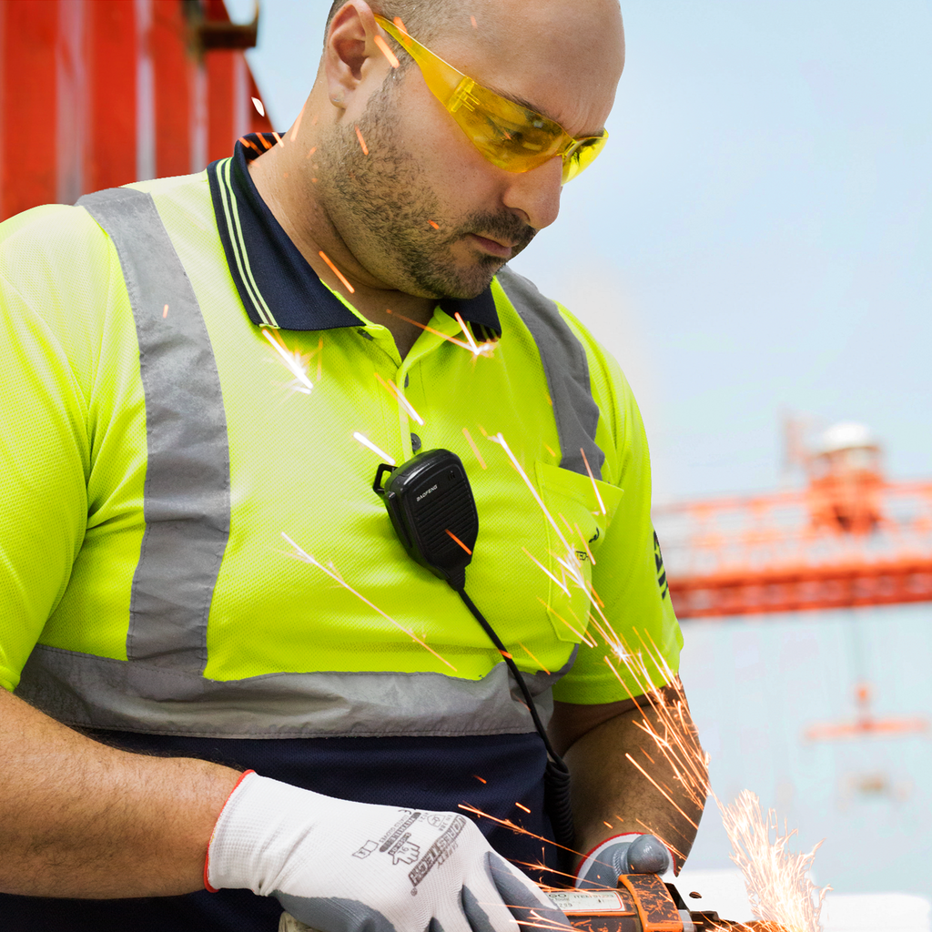 A man wearing a high visibility polo shirt, white protective gloves and the all yellow JORESTECH ANSI compliant safety glasses while working in a workshop with a power machine